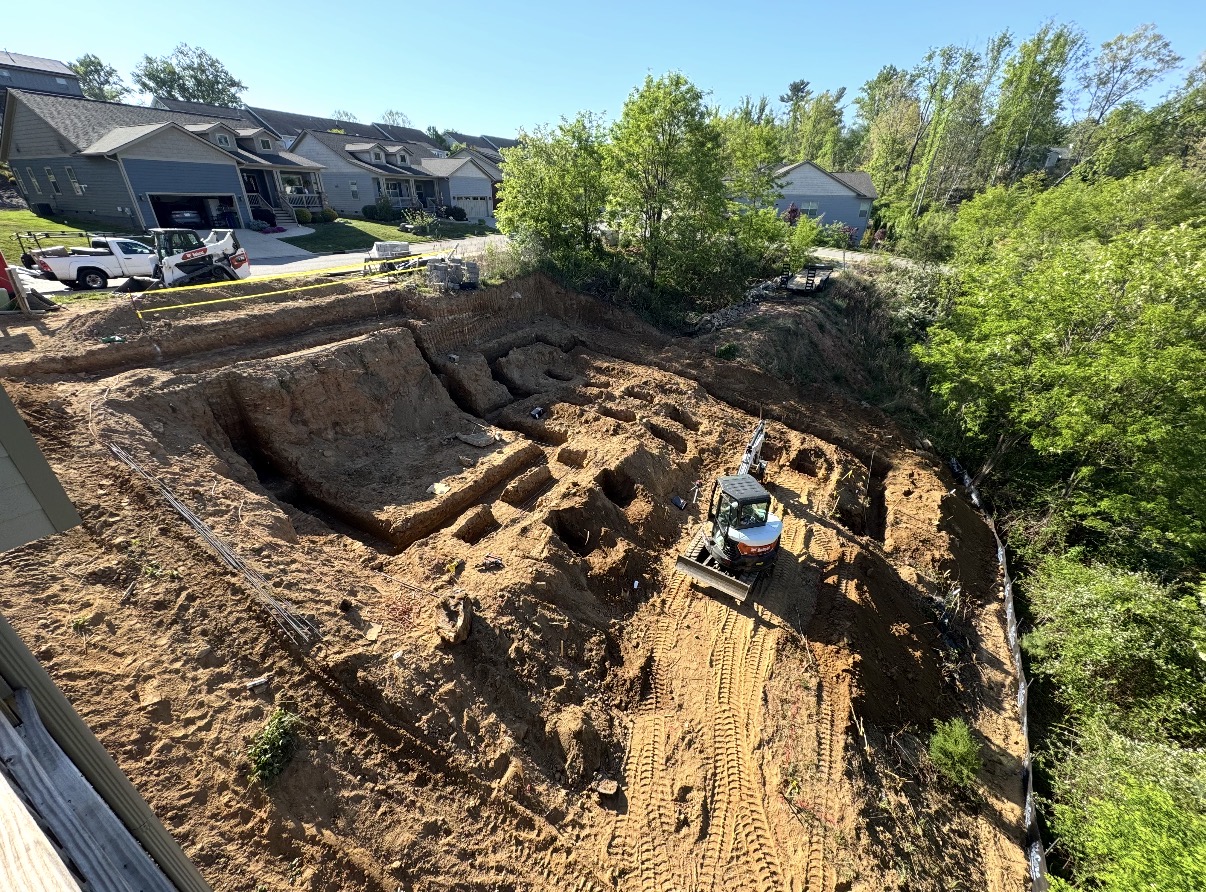 Excavator grading and digging out a foundation footprint in a neighborhood